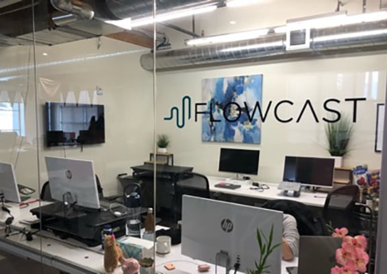 Shared office space behind a glass-walled conference room displaying Flowcast's logo
