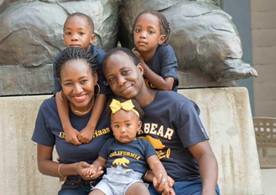 Kadidia Konate poses for a family photo in front of the Cal Bear statues with her husband, baby daughter, and twin son and daughter. All wear blue and gold UC Berkeley t-shirts.